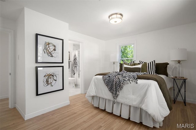 bedroom featuring baseboards, light wood finished floors, and connected bathroom