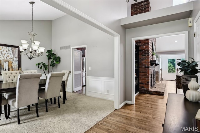2113 Fairway Bnd, Chesterfield, MO 63017 - dining space featuring a chandelier, high vaulted ceiling, wood finished floors, a brick fireplace, and wainscoting