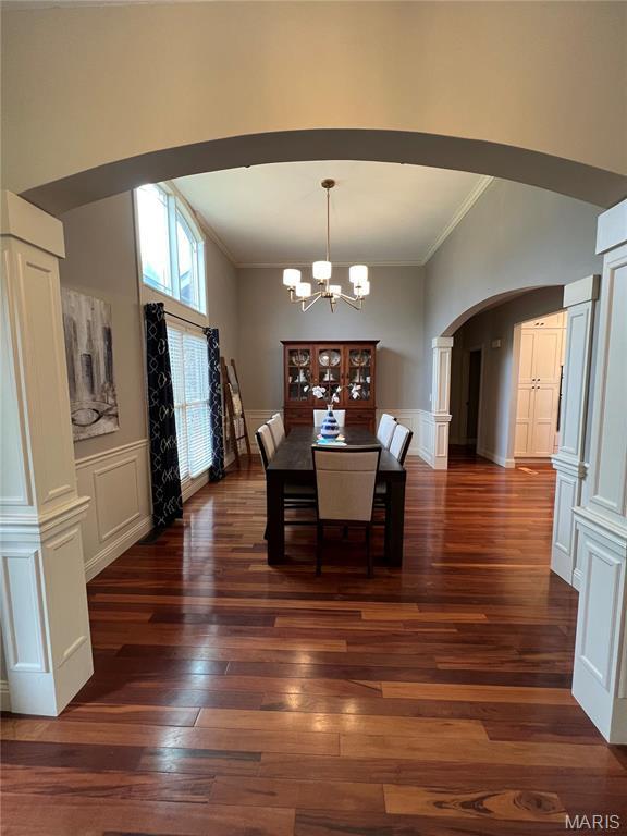 dining area featuring arched walkways, ornamental molding, a chandelier, dark wood finished floors, and a decorative wall