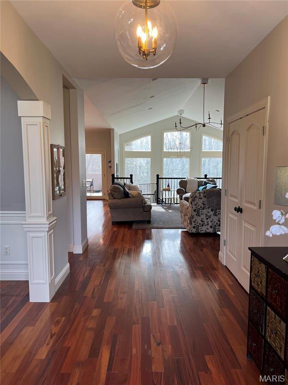 corridor featuring a chandelier, wood finished floors, vaulted ceiling, and baseboards