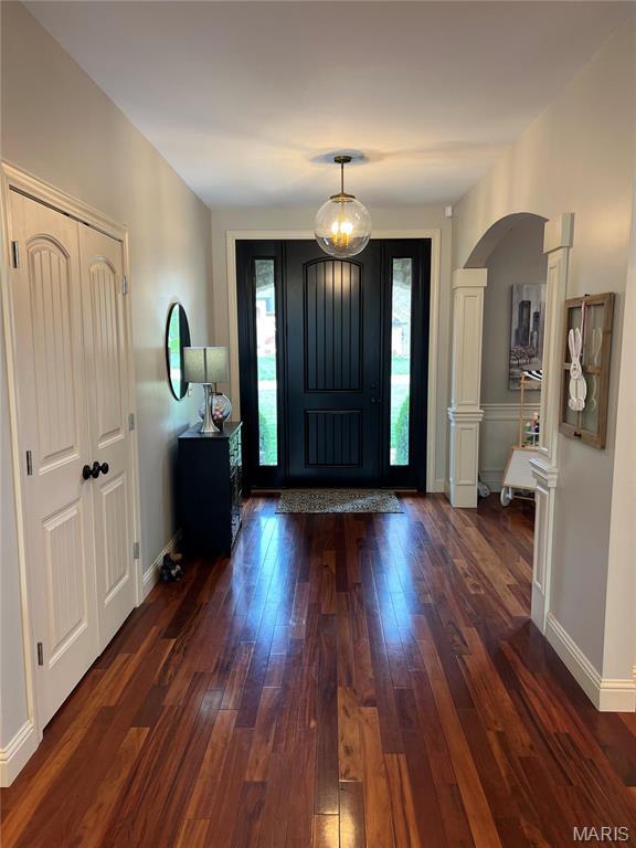 entryway with dark wood-style flooring, arched walkways, baseboards, and decorative columns