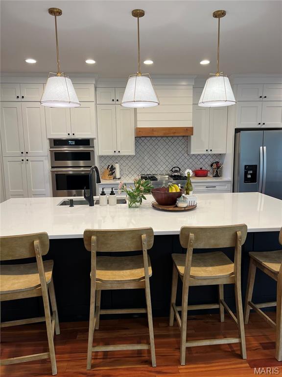 kitchen with appliances with stainless steel finishes, light countertops, hanging light fixtures, and wood finished floors