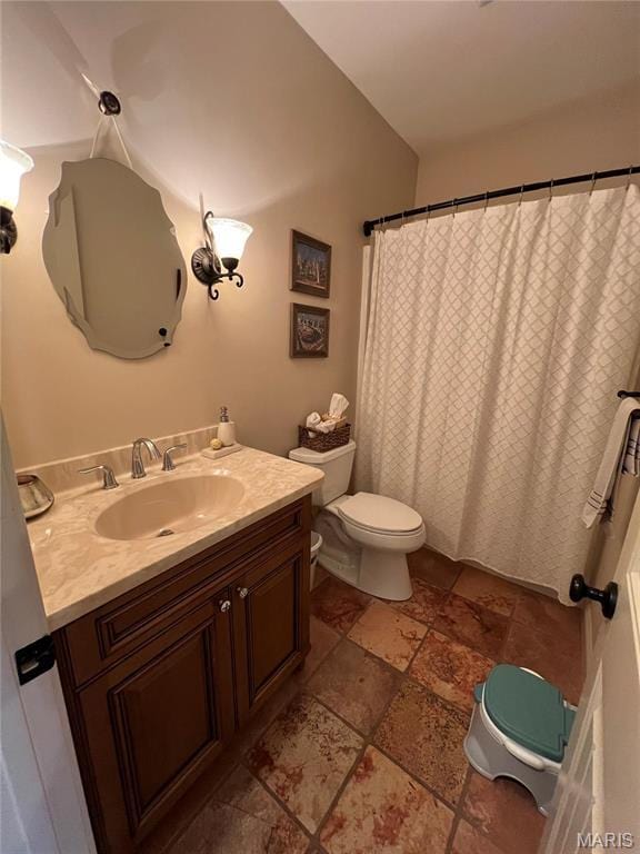 full bath with stone tile floors, vanity, toilet, and a shower with shower curtain