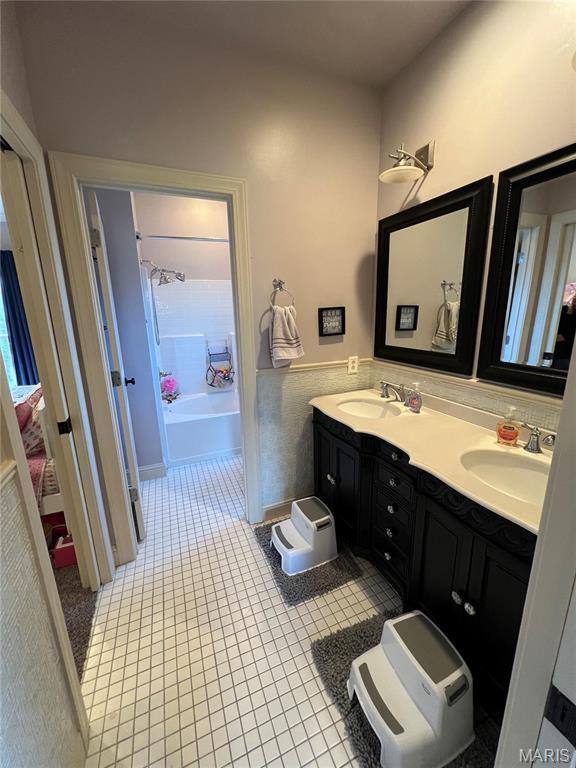 bathroom with tile patterned flooring, double vanity, a bath, and wainscoting