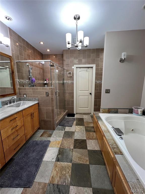 full bathroom featuring a shower stall, a chandelier, tile walls, a jetted tub, and vanity