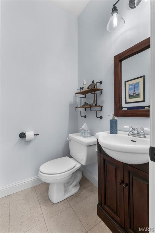 half bath with baseboards, toilet, vanity, and tile patterned flooring
