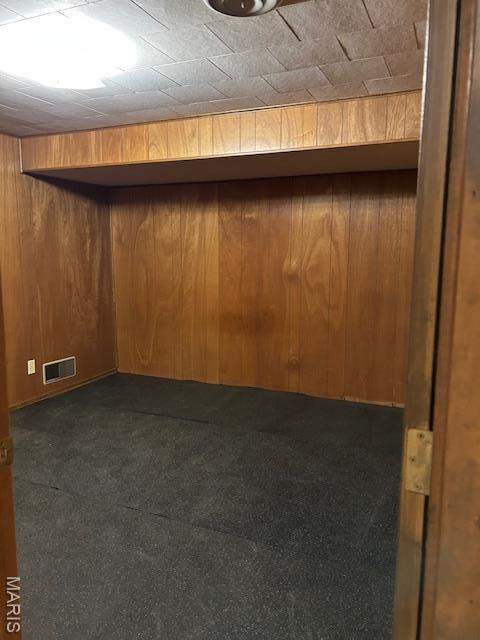 finished basement featuring dark carpet and wooden walls