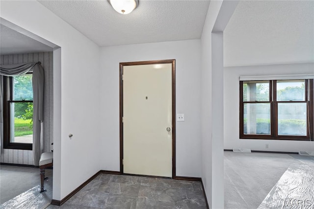 carpeted entryway featuring a textured ceiling and baseboards