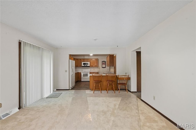 kitchen with white appliances, brown cabinetry, a peninsula, light countertops, and a kitchen bar