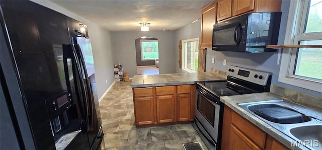 12753 Hencher Rd, De Soto, MO 63020 - kitchen featuring black appliances, a peninsula, brown cabinetry, a sink, and arched walkways