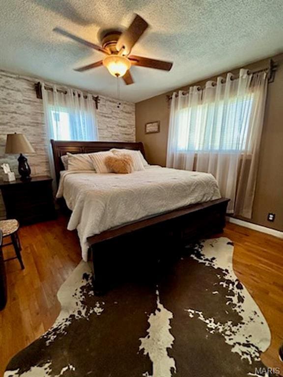 bedroom with a textured ceiling, multiple windows, wood finished floors, and ceiling fan