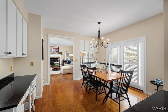 1114 Lockett Rd, Des Peres, MO 63131 - dining area featuring a fireplace, light wood finished floors, a chandelier, and baseboards