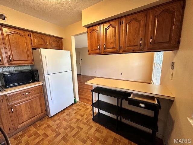 8736 Santa Bella Dr Unit G, Hazelwood, MO 63042 - kitchen with freestanding refrigerator, black microwave, light countertops, brown cabinetry, and a textured ceiling