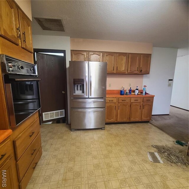 23026 Reporter Rd, Waynesville, MO 65583 - kitchen with stainless steel fridge with ice dispenser, oven, brown cabinets, a warming drawer, and a textured ceiling