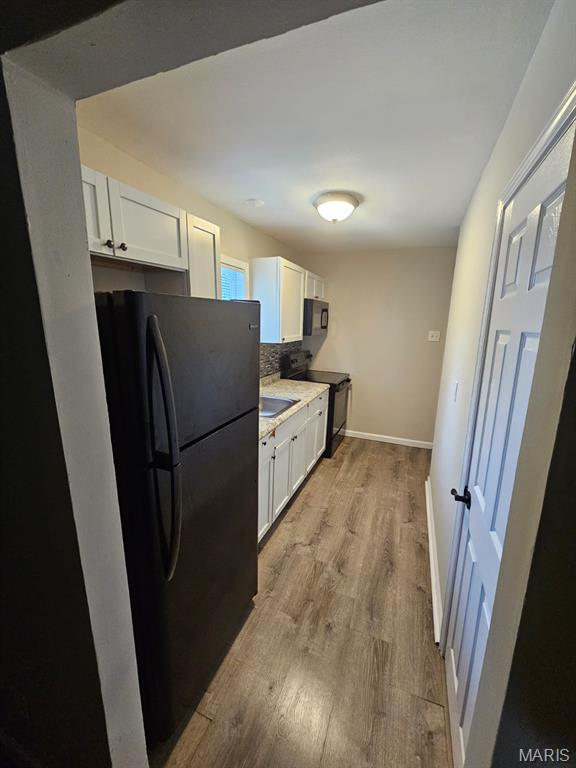 7200 Sapphire Ave, Saint Louis, MO 63136 - kitchen with black appliances, white cabinetry, backsplash, light wood-type flooring, and light countertops