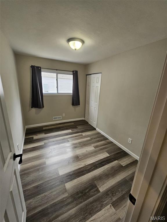 9827 Winkler Dr, Saint Louis, MO 63136 - unfurnished bedroom featuring dark wood-type flooring, a closet, baseboards, and a textured ceiling