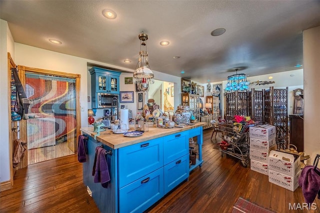 20955 Rye Ln, Richland, MO 65556 - kitchen with wooden counters, blue cabinetry, stainless steel microwave, dark wood-style flooring, and hanging light fixtures