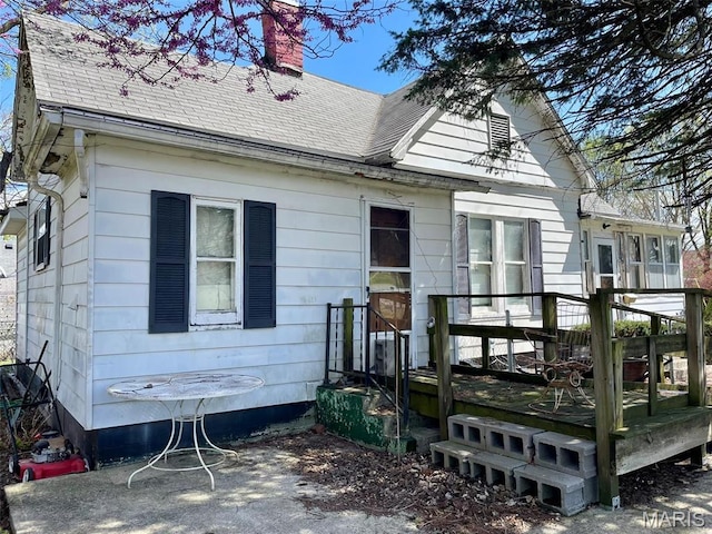 back of house featuring a deck, a shingled roof, and a chimney