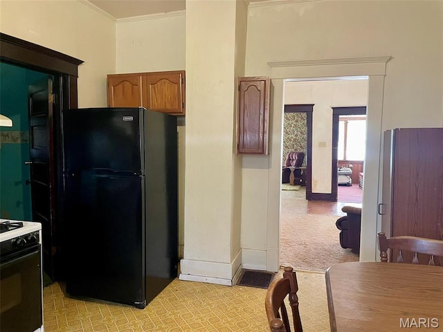 kitchen featuring freestanding refrigerator, light colored carpet, gas stove, baseboards, and ornamental molding