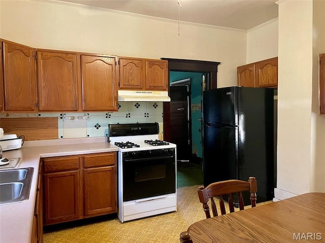 kitchen featuring gas stove, freestanding refrigerator, under cabinet range hood, light countertops, and brown cabinets