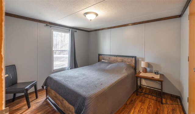 bedroom featuring wood finished floors, ornamental molding, baseboards, and a textured ceiling