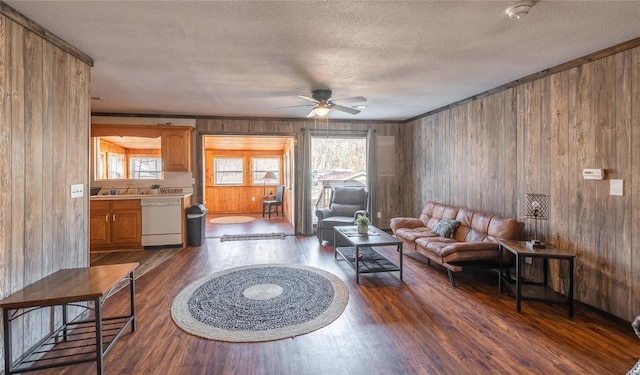 living area with a textured ceiling, dark wood-style floors, ceiling fan, and wooden walls