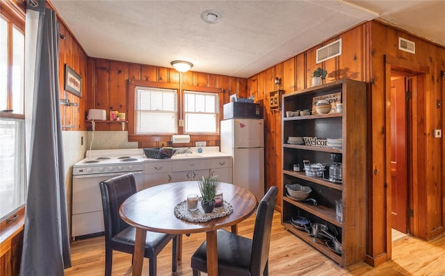 kitchen featuring white appliances, light wood-type flooring, wooden walls, a textured ceiling, and light countertops