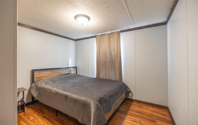 bedroom with wood finished floors, baseboards, a textured ceiling, and crown molding