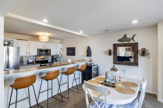 kitchen with appliances with stainless steel finishes, carpet floors, a breakfast bar area, white cabinetry, and backsplash