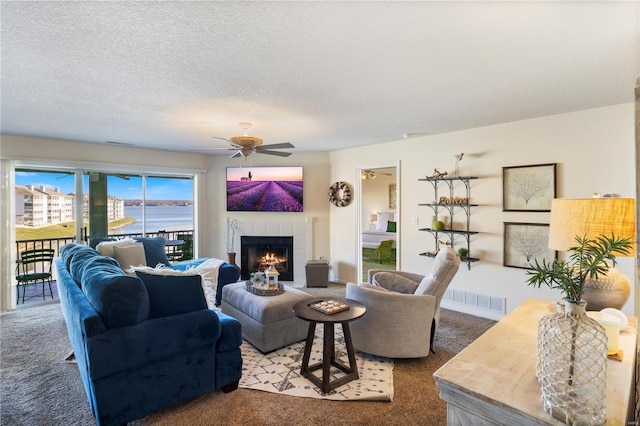 living area featuring carpet floors, a tiled fireplace, a ceiling fan, and a textured ceiling