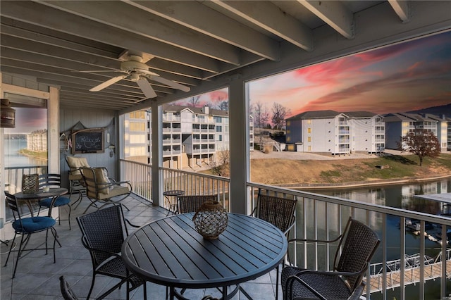 balcony at dusk with a ceiling fan, a water view, and outdoor dining area
