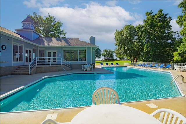 community pool with french doors, a patio area, and fence