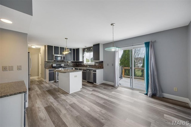 1008 Baypointe Dr, Imperial, MO 63052 - kitchen with appliances with stainless steel finishes, light wood-style flooring, a kitchen island, decorative backsplash, and dark countertops