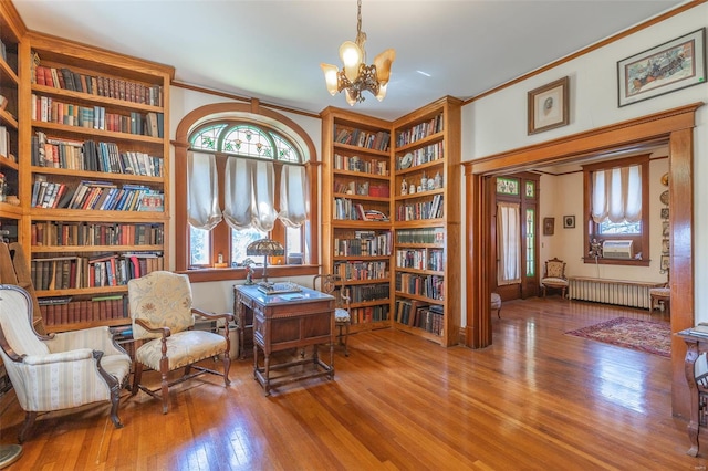 living area with radiator, a chandelier, bookshelves, wood finished floors, and crown molding