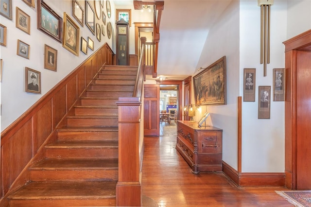 staircase with wood finished floors, wainscoting, and a towering ceiling