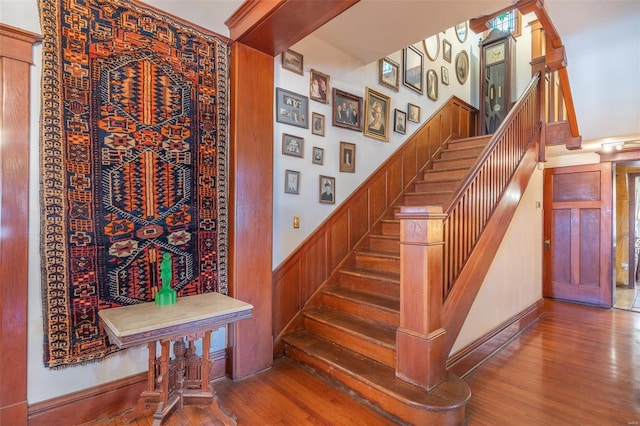 stairway with wood finished floors and a wainscoted wall