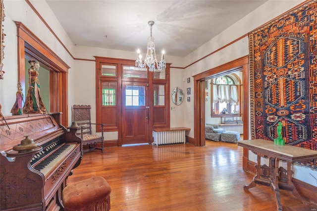 foyer entrance featuring radiator, a chandelier, wood finished floors, and healthy amount of natural light