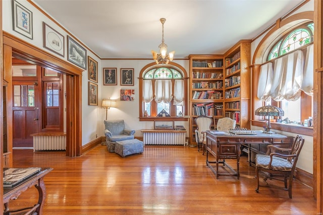 living area with radiator heating unit, a chandelier, plenty of natural light, wood-type flooring, and ornamental molding