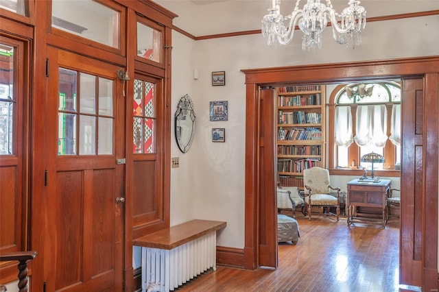 foyer with wood finished floors, ornamental molding, a chandelier, and baseboards