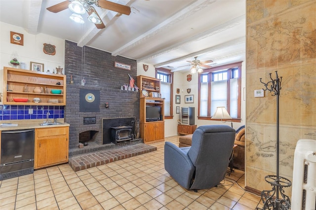 living area featuring ceiling fan, beamed ceiling, a wood stove, and light tile patterned floors