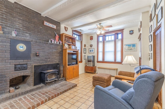 living room featuring radiator, beamed ceiling, light tile patterned floors, ceiling fan, and a wood stove