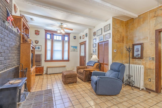 sitting room featuring radiator heating unit, light tile patterned floors, beamed ceiling, ceiling fan, and a wood stove