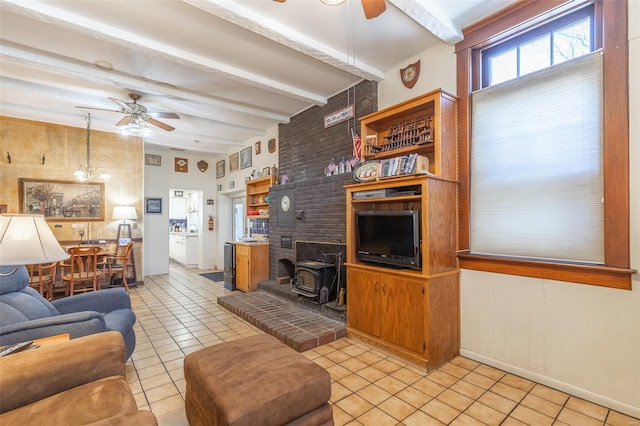 living room with ceiling fan, a wood stove, light tile patterned flooring, beam ceiling, and baseboards