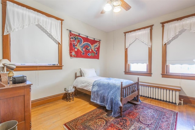 bedroom featuring radiator, wood finished floors, baseboards, and ceiling fan