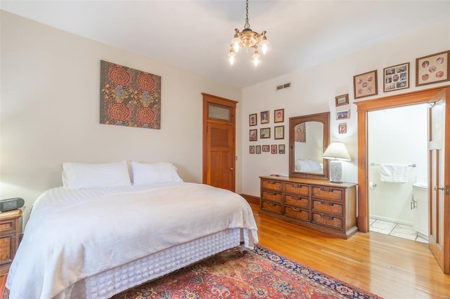 bedroom with light wood finished floors, a chandelier, and connected bathroom