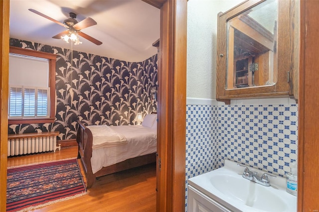 bathroom featuring radiator heating unit, wallpapered walls, wood finished floors, ceiling fan, and vanity