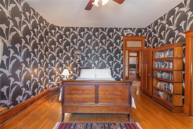 bedroom with wallpapered walls, an accent wall, wood finished floors, and baseboards