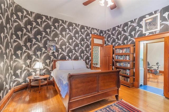bedroom featuring wallpapered walls, an accent wall, hardwood / wood-style flooring, and baseboards