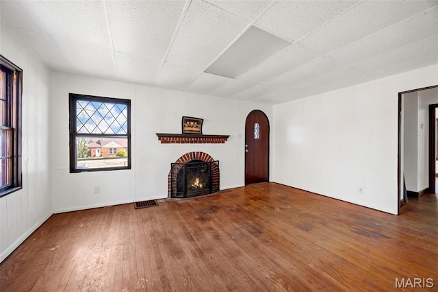 1825 S New Florissant Rd, Florissant, MO 63031 - unfurnished living room featuring wood-type flooring, a brick fireplace, arched walkways, and a drop ceiling