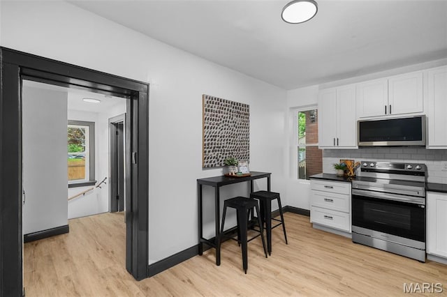 6007 S Kingshighway Blvd S, Saint Louis, MO 63109 - kitchen featuring stainless steel appliances, white cabinetry, light wood-type flooring, decorative backsplash, and dark countertops